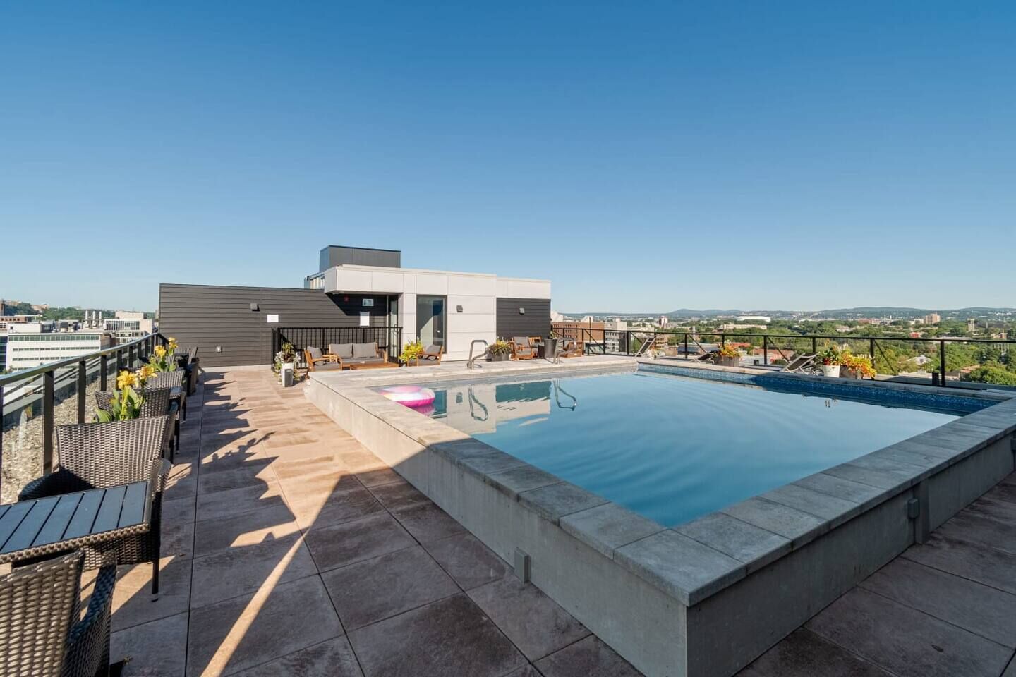 A rooftop pool with a modern building in the background, surrounded by outdoor seating and a clear view of the cityscape.