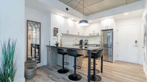 Uma cozinha moderna com ilha central, banquetas e uma geladeira de aço inoxidável.