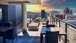 Terraço no terraço com área de estar externa, lareira e vista da cidade ao pôr do sol.
