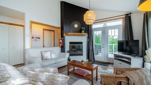 A modern living room with a sofa, a coffee table, a fireplace, a television, and a large window with curtains. - Panoramic View: 2BR + FP + BBQ + Terrace - Upper (Petite-Rivière-Saint-François)