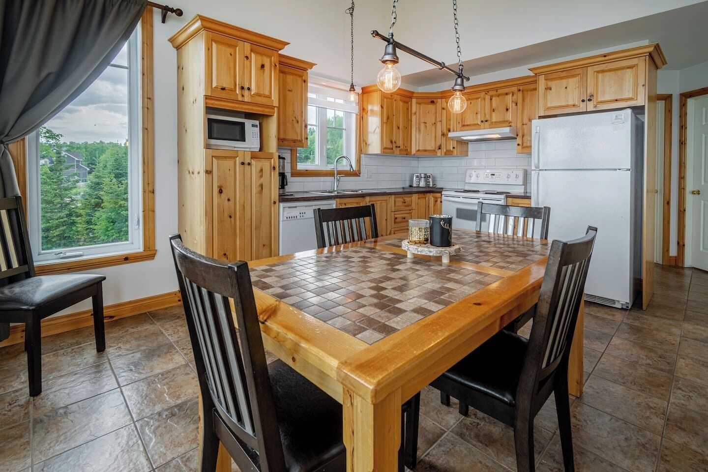A kitchen with wooden cabinets, a large dining table, and hanging pendant lights.