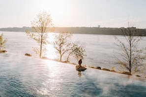 A serene riverside setting with a person sitting on a rock, trees, and a distant city skyline. - Loft | Smart TV + kitchen + Gym | 98 Walkscore (Québec City)