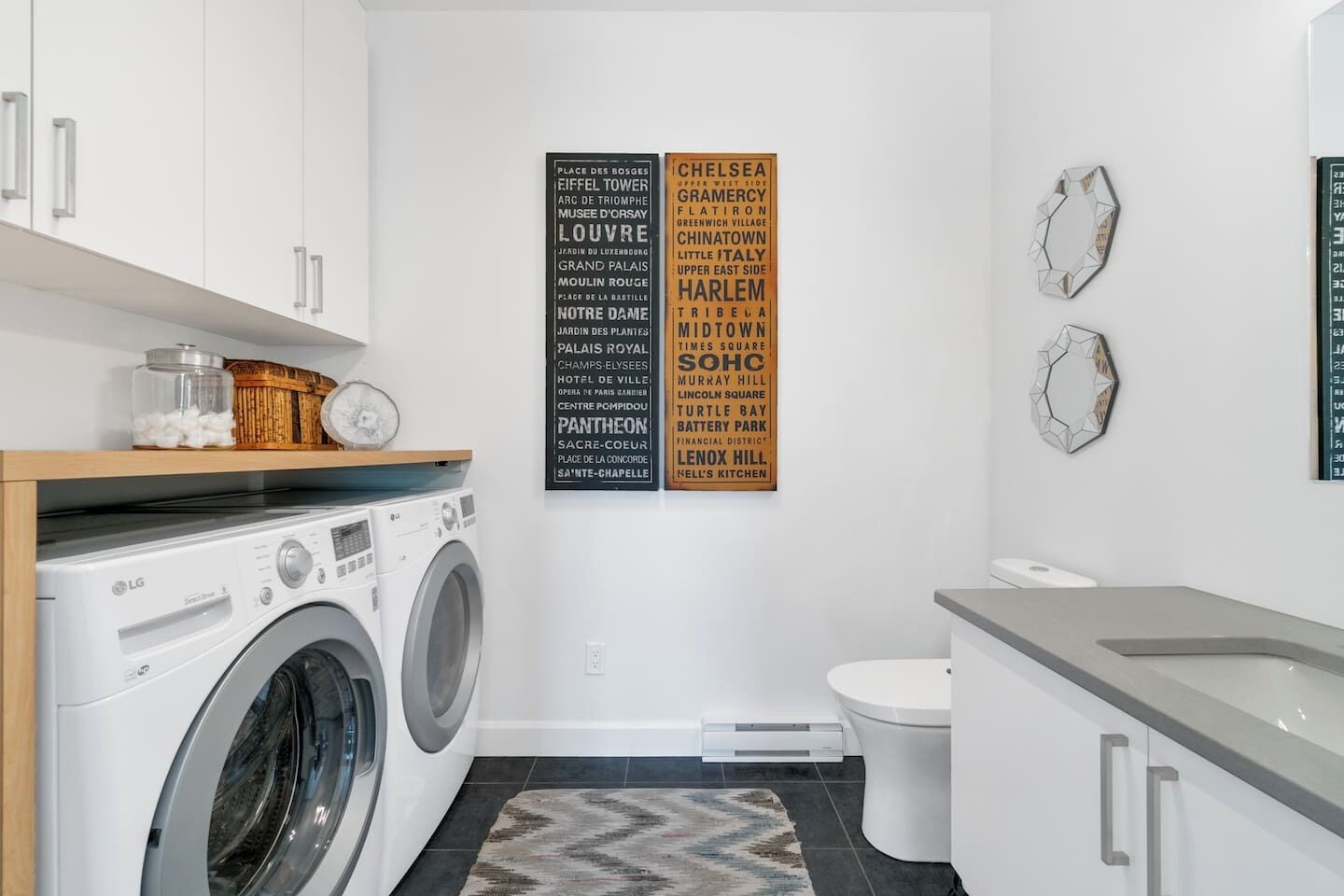 Une buanderie moderne équipée d’un lave-linge et d’un sèche-linge à chargement frontal, d’une petite étagère avec des bocaux et d’un miroir fixé au mur.