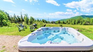 Un jacuzzi en un área con césped, sillas y vistas a las colinas.