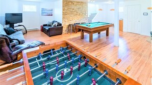 Una sala de estar con mesa de futbolín, mesa de billar, sofá y televisión.