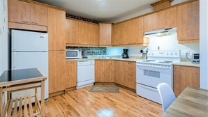 A compact kitchen with wooden cabinets, a microwave, a dishwasher, a stove, and a small dining table. - Charming Condo - Perfect for Visiting Quebec City (Québec City)