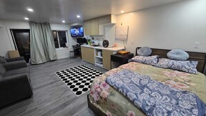 Camera d'albergo moderna con un letto, una poltrona, un angolo cottura e una televisione.