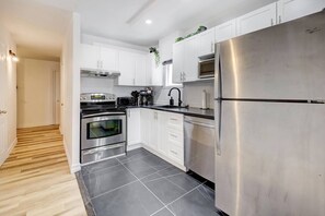 Une cuisine moderne dotée d’appareils électroménagers en acier inoxydable, de meubles blancs et d’un sol carrelé.