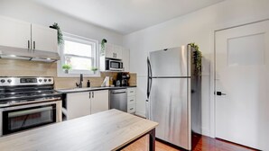 A modern kitchen with stainless steel appliances, a wooden table, and white cabinetry.