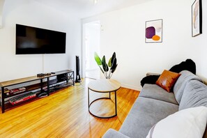 A living room with a grey sofa, a coffee table, a flat-screen TV, and a bookshelf. - Modern 2BR Quebec City | 10 min Old Quebec | Patio (Québec City)