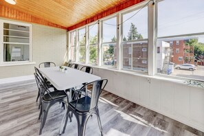 A dining area with a white table and black chairs, large windows, and a view of a residential street. - Modern 2BR Quebec City | 10 min Old Quebec | Patio (Québec City)