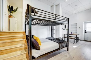 Ein Schlafraum mit Etagenbetten, einer Holztreppe, einem kleinen Tisch mit Stuhl und einer Pflanze an der Wand.