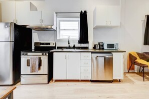 Eine moderne Küche mit weißen Schränken, Edelstahlgeräten, einem schwarzen Geschirrtuch an dem Backofen und einer Mikrowelle auf der Arbeitsplatte.
