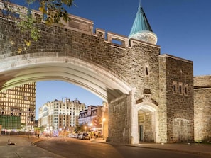 Eine Steinbogenbrücke über einer Straße, im Hintergrund moderne Gebäude.