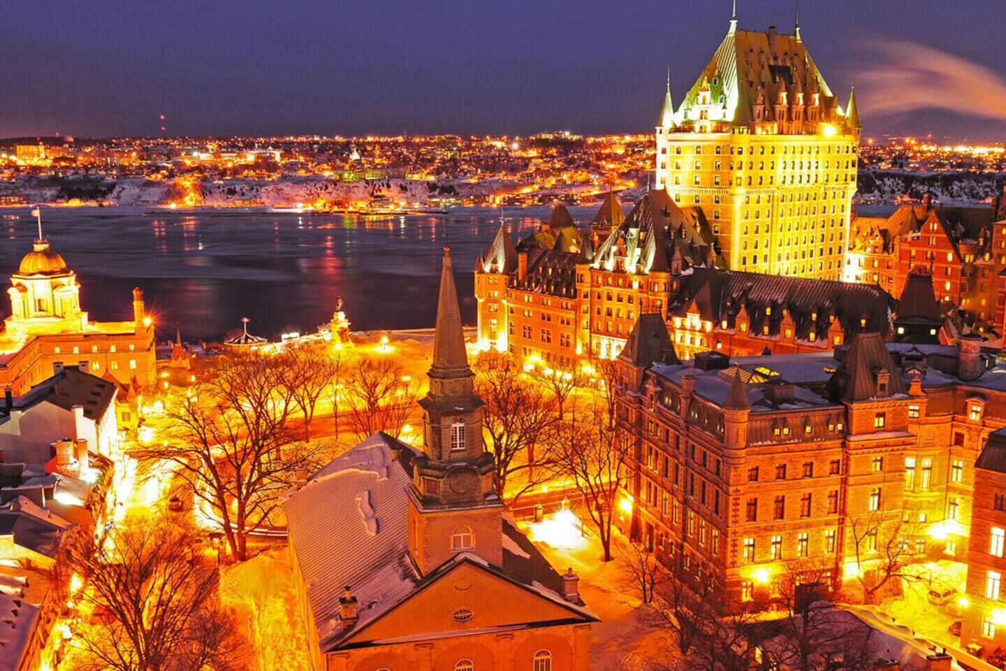A historic building with a prominent tower and spires, surrounded by other buildings and a body of water.