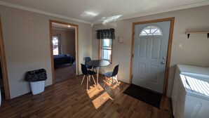 Un espacio habitable compacto con comedor, una puerta con ventana y un cesto de basura visible.