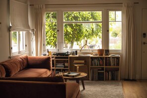 Ein gemütliches Wohnzimmer mit einem braunen Sofa, einem Couchtisch, einem Bücherregal und einem Fenster mit Vorhängen.