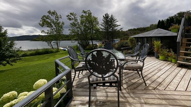 Une terrasse en bois, agréée de mobilier d’extérieur, qui offre une vue sur un lac et la verdure environnante.
