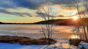 Un lac gelé, bordé d’arbres sans feuilles, avec un coucher de soleil en arrière-plan.