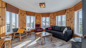 Una sala de estar acogedora con paredes de madera, ventanas grandes, un sofá, un sillón y una mesa de centro.