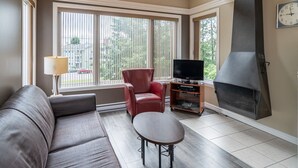 A living room with a sofa, a red chair, a TV on a wooden stand, and a large fireplace.