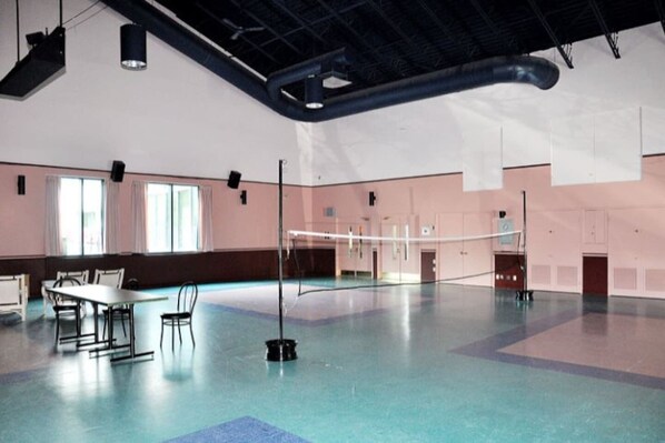 A spacious indoor area with a high ceiling, a volleyball net, and a table with chairs.