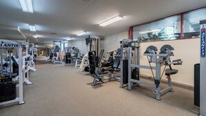 Un gimnasio con diversas máquinas de ejercicio, bancos de pesas y pesas libres, distribuidas en un espacio amplio.