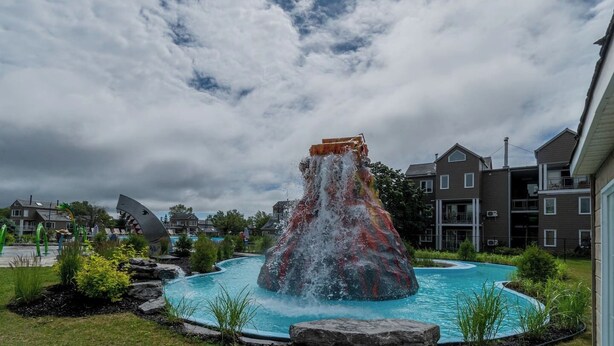 Una fuente de agua con cascada y piscina, rodeada de follaje y edificios residenciales.