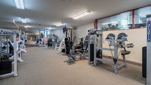 Un gimnasio con diversas máquinas de ejercicio, bancos de pesas y pesas libres, distribuidas en un espacio amplio.