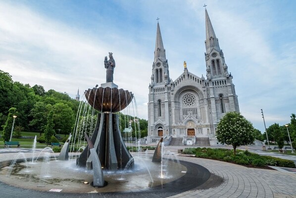 Une grande église dotée de deux flèches jumelles et d’une rosace centrale, entourée d’une fontaine et de verdure.
