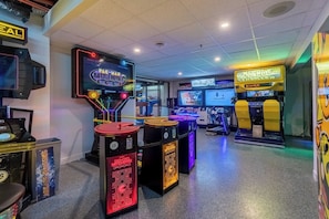 A gaming arcade with various machines, including Pac-Man Battle Royale, and a neon-lit sign.
