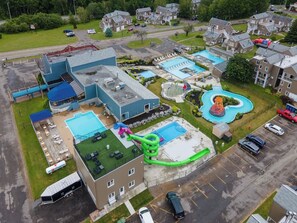 Vue aérienne d’un quartier résidentiel avec plusieurs piscines, un grand toboggan aquatique et un parking.