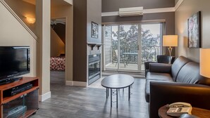 A modern living room with a flat-screen TV, a sofa, a coffee table, and a fireplace. - MSA condo with year-round heated pool and spa! (Beaupré)