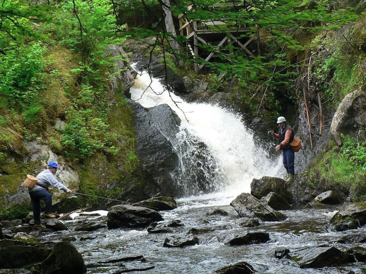 A natural setting with a waterfall and two individuals engaged in an outdoor activity.