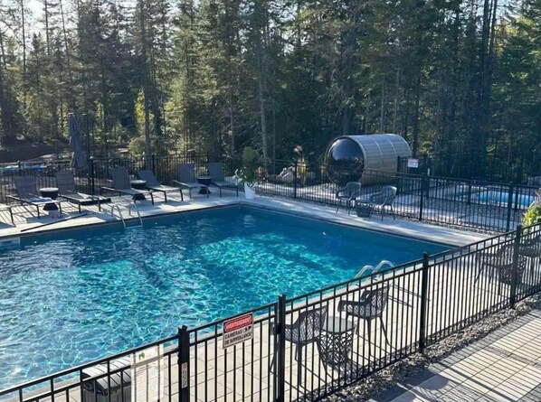 A swimming pool with a metal barrel structure, surrounded by a fence and chairs, set in a forested area.