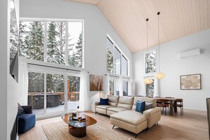 A spacious living room with large windows, a high ceiling, and a cozy seating area.