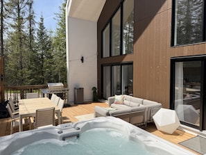 A modern outdoor patio with a hot tub, seating area, and a barbecue grill.