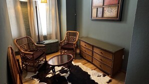 Een gezellige kamer met een kussen van runderleer, rieten meubels en een groot abstract schilderij.
