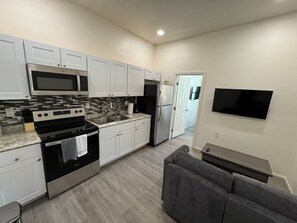 A modern kitchen with white cabinets, a stainless steel stove, and a built-in microwave. - Historic Broad St Apt in Upton’s Confectionery (Globe)