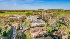A rural property with multiple buildings, including a main house and several outbuildings, surrounded by fields and trees. - Charming Family Stables Conversion - Pass the Keys (Emsworth)