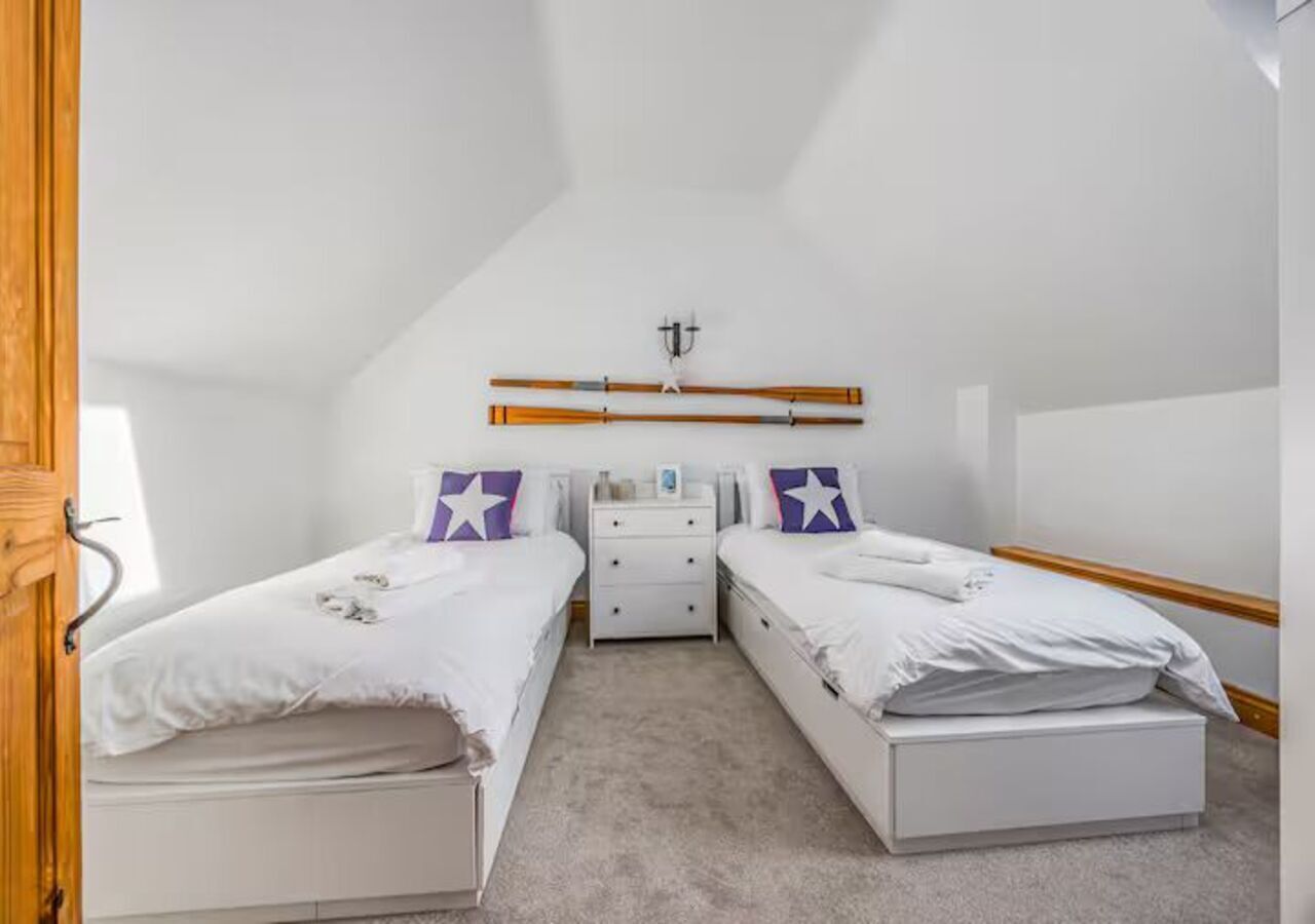 A small, well-lit room with two single beds, a nightstand, and a dresser.