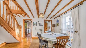 A dining area with a round table, wooden chairs, and a staircase with wooden railings. - Charming Family Stables Conversion - Pass the Keys (Emsworth)