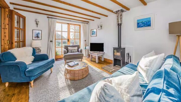 A cozy living room with a blue sofa, a round coffee table, and a fireplace. - Charming Family Stables Conversion - Pass the Keys (Emsworth)
