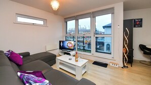 Un salon moderne avec un canapé, une table basse, un téléviseur et de grandes fenêtres donnant sur la ville.