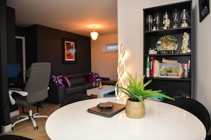 A modern living room with a white round table, a grey office chair, a black sofa, a small white side table, a potted plant, and a bookshelf with decorative items. - Cardiff Bay Retreat, Sleeps 4 & Parking! - Pass the Keys (Cardiff)