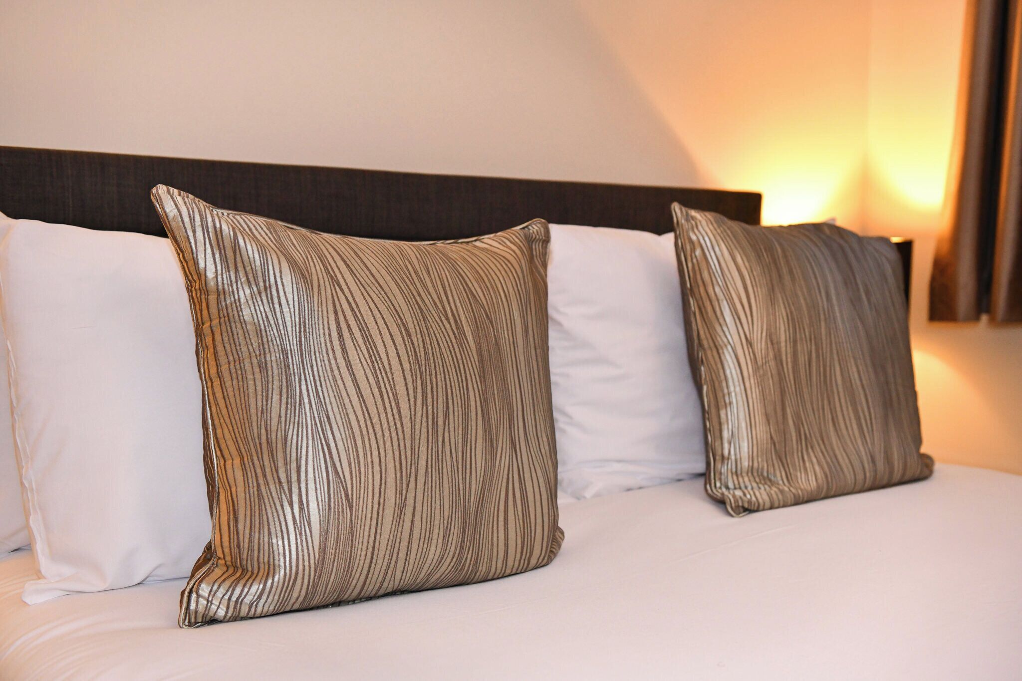 A bed with two striped pillows and a plain pillow.