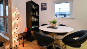Une pièce moderne avec une table ronde, des chaises noires, une bibliothèque, un élément décoratif mural et une fenêtre donnant sur un beau paysage.
