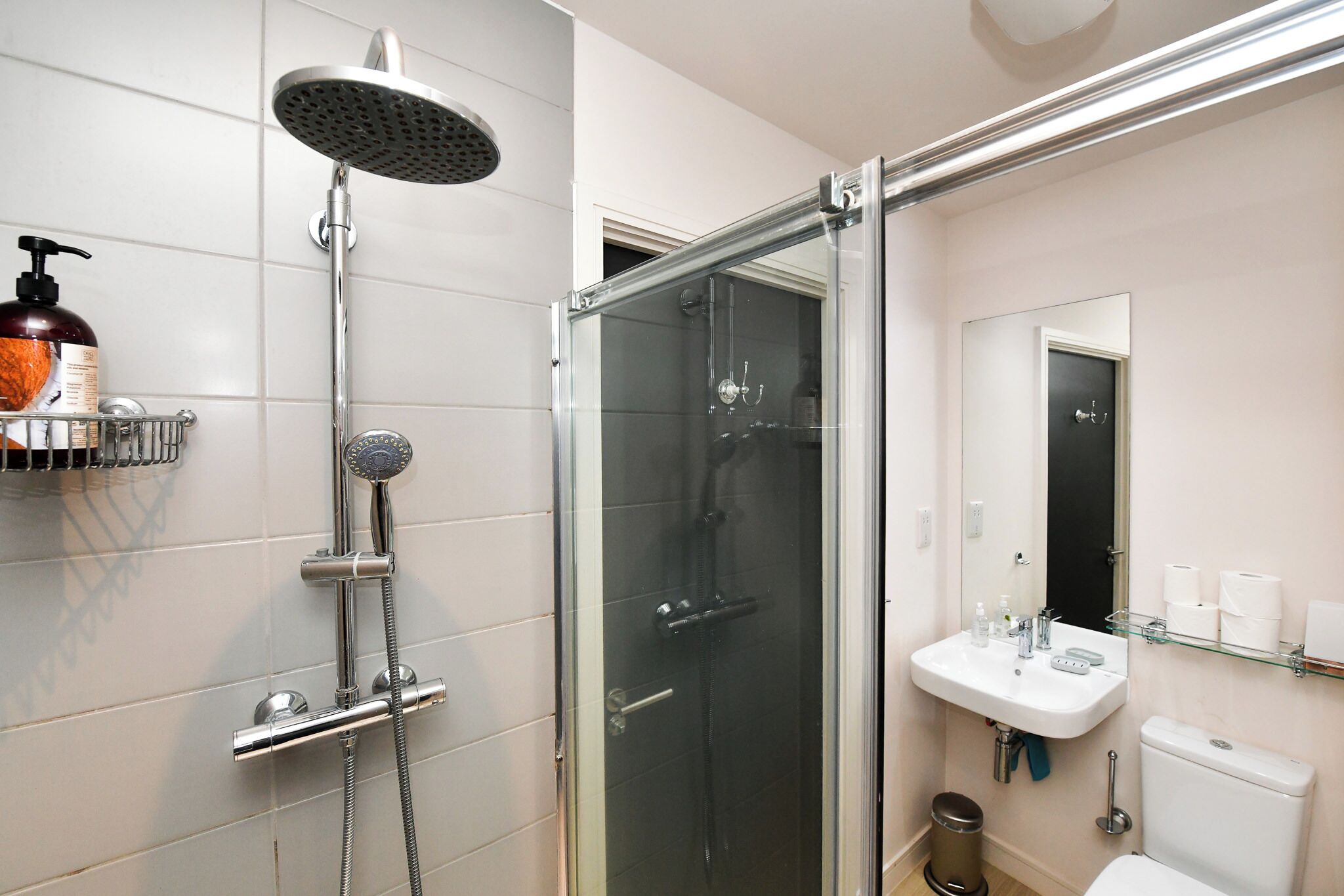 Een moderne badkamer met een douchecabine van glas, een witte wastafel en een toilet.