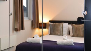 Une chambre d’hôtel avec un lit, des oreillers, une lampe de chevet et une fenêtre avec des rideaux.