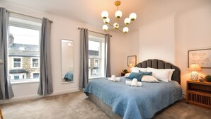 Een slaapkamer met een groot bed, een kroonluchter, uitzicht door het raam en een spiegel aan de muur.